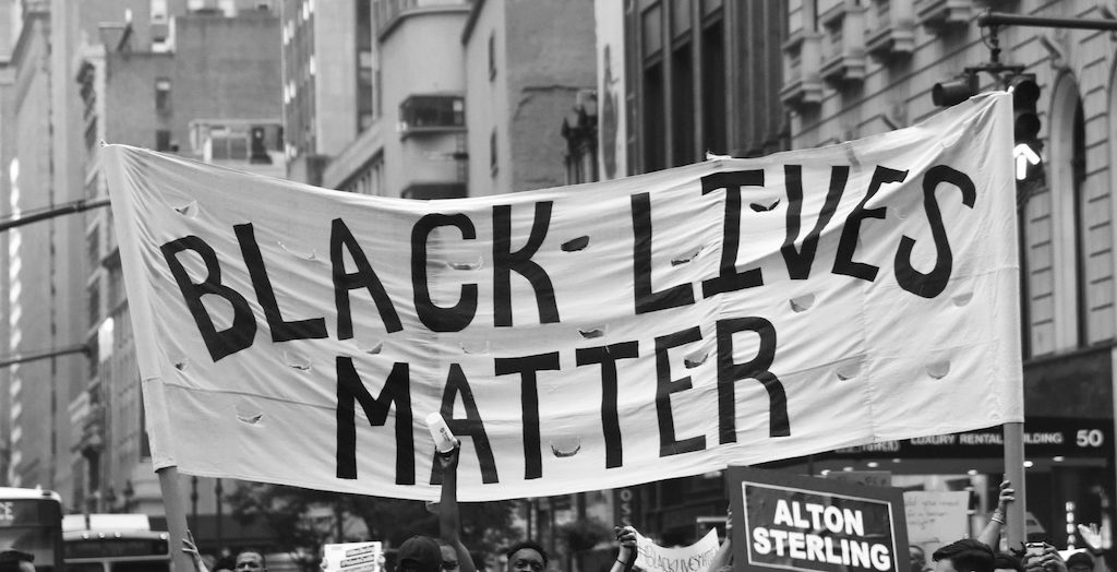 A black and white photo of a Black Lives Matter banner held up at a protest.